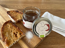 Lade das Bild in den Galerie-Viewer, Ein Glas Chili in Honig auf einem Holzbrett mit einem gerösteten feinen Dinkelbrot mit Chilihonig und einer kleinen Prise Salz.