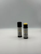 Zwei Sticks Bio Lippenpflege Wohltat stehen nebeneinander einmal mit und einmal ohne Deckel. Das Etikett ist schlicht gehalten mit Logo, Waben und der Beschreibung.