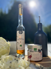 Lade das Bild in den Galerie-Viewer, Eine Flasche Kramerhonig Weißer Honig-Balsamico, Glas Kramerhonig Chili in Honig und eine Flasche Olivenöl auf einem Holzbrett mit Weißkraut auf einem sonnigen Gartentisch
