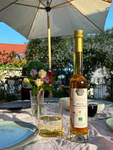 Lade das Bild in den Galerie-Viewer, Sommerliches Gartenambiente mit Sonnenschirm und gemütlich gedecktem Tisch. Verzehrtipp: Kramerhonigs Weisser Honigbalsamico steht neben einem glas Wasser in dem ein Spritzer Essig ist und zeigt die Erfrischung.
